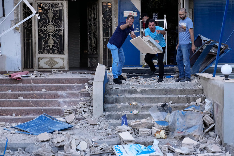 Libaneser städar undan rasmassor som störtat ned framför en butik på bottenvåningen i det hus som attackerades i Beirut under natten till måndag.