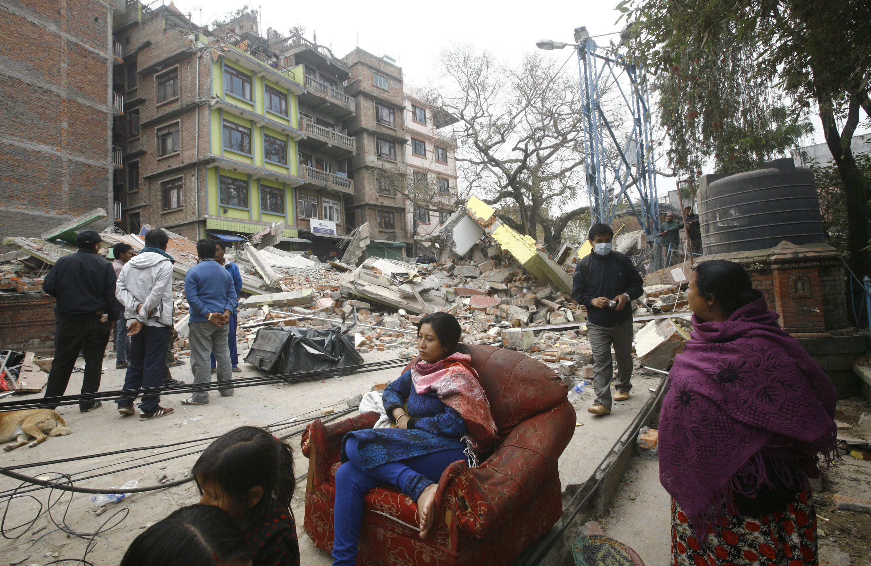 En nepalesisk kvinna sitter i en fåtölj mitt bland förstörelsen.