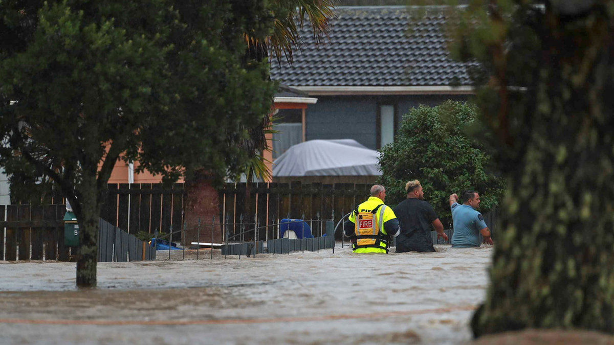 Personal från räddningstjänsten och en civilperson vadar genom vattenmassorna i Auckland på fredagen.