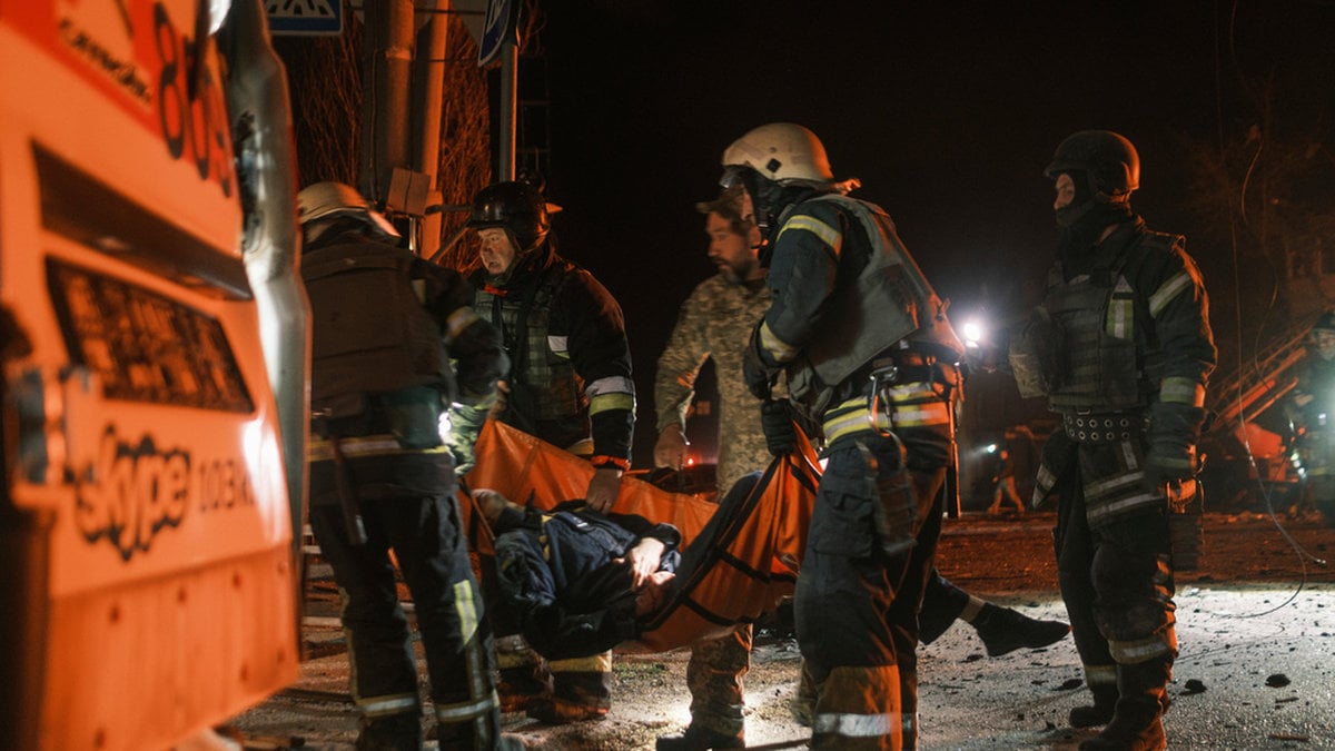 Ukrainska räddningsarbetare i Charkiv bär bort kvarlevorna efter en kollegat som dödats i en rysk attack.