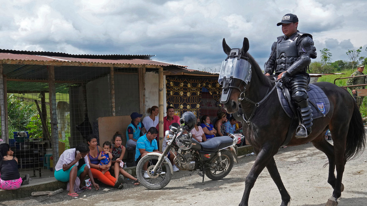 En ridande polis passerar människor som väntar utanför Bellavista-fängelset i Ecuador för att få information om sina anhöriga.