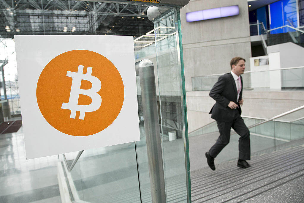Bild på bitcoinmärket på en glasvägg samt en man i kostym.