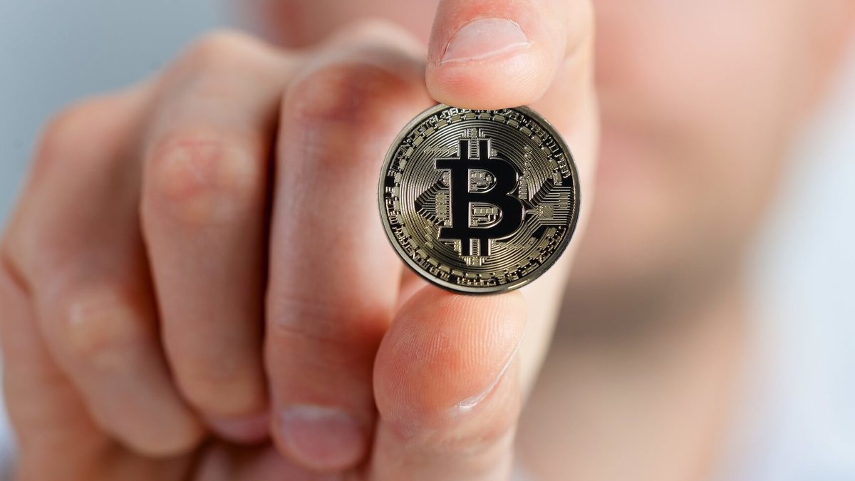 En bild på en hand som håller upp ett bitcoin-mynt.