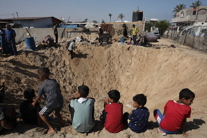 Barn sitter vid en krater som bildats av en israelisk bomb mot Khan Yunis. Bild tagen i juni.