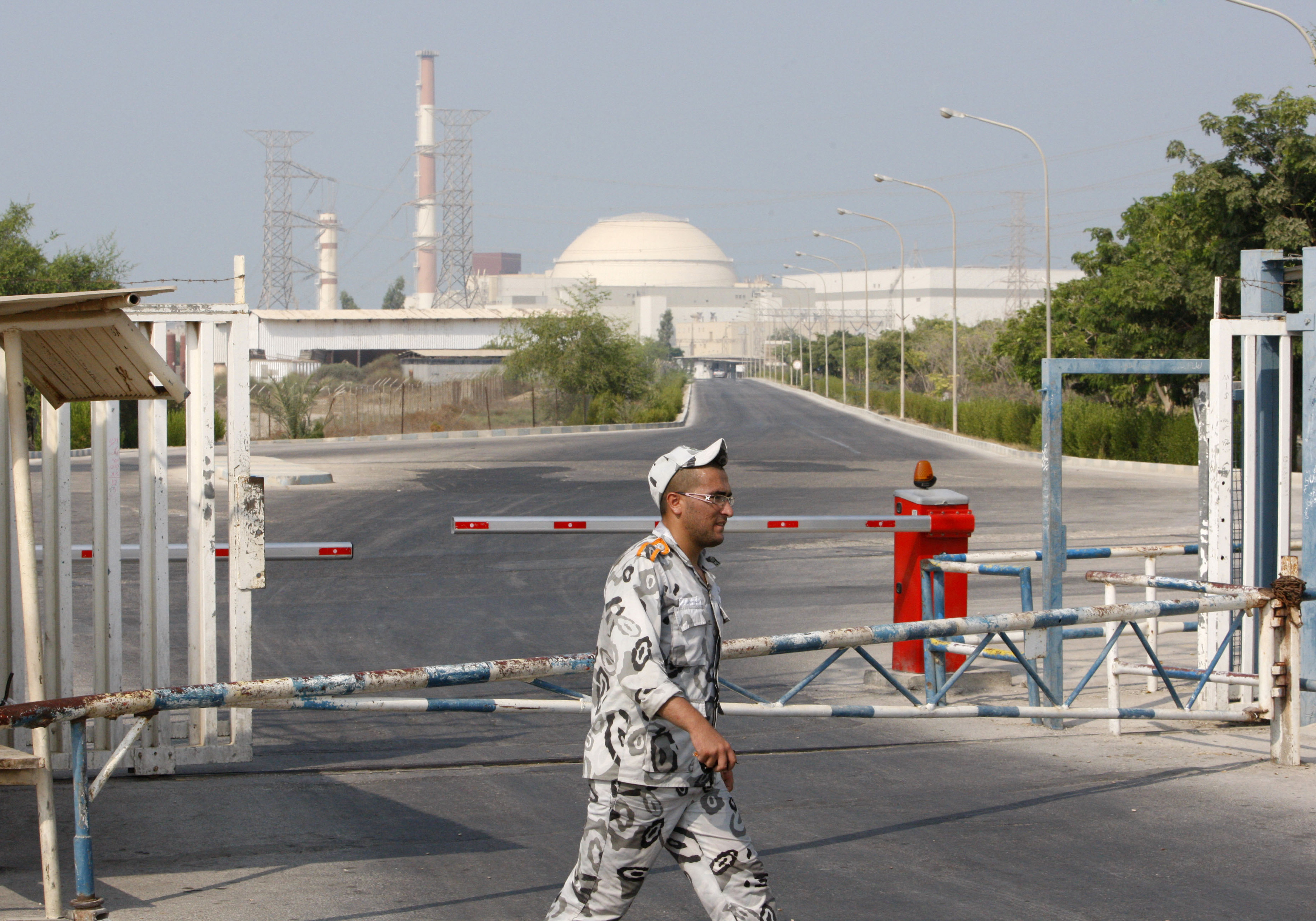 En vakt patrullerar framför porten in till Buhsehr-kraftverket i Iran, byggnaden som ses i bakgrunden.