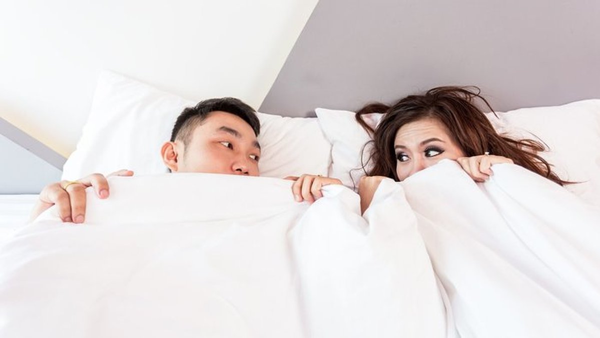 En man och en kvinna ligger i en säng med täcket överdraget över halva ansiktet.