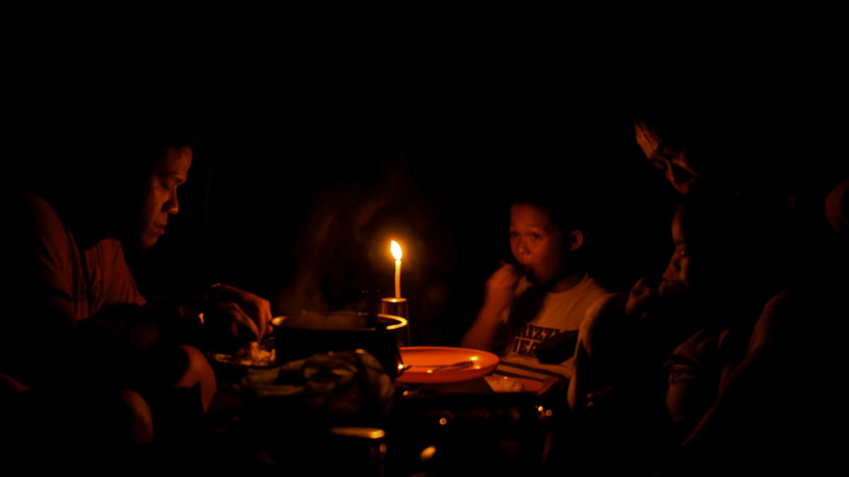 En familj i Filippinerna samlas kring hemmets enda ljuskälla och delar på en måltid.