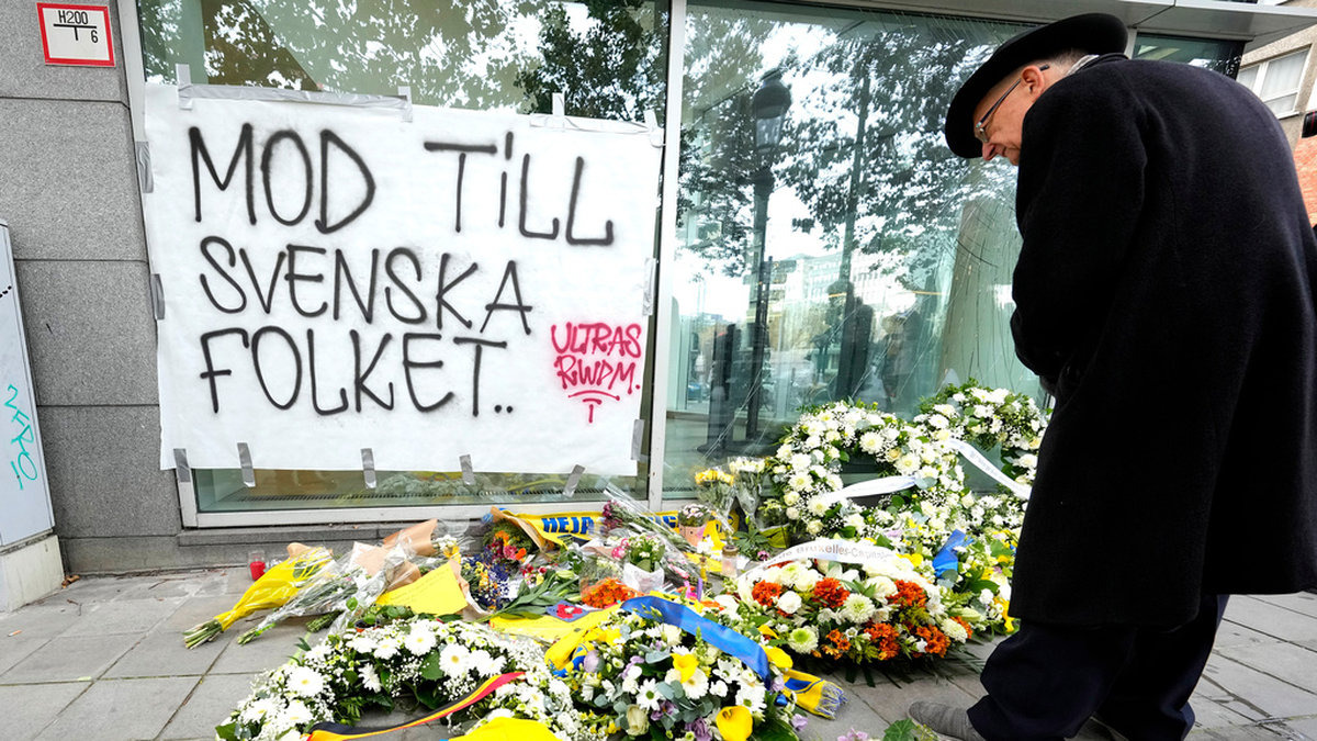 En man studerar blommor, kransar och fotbollskläder som lagts ned vid brottsplatsen i Bryssel där två svensk supportrar sköts till döds i måndags.