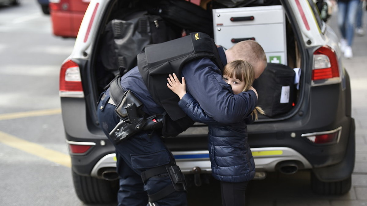 En polis kramar om ett barn framför en polisbil.