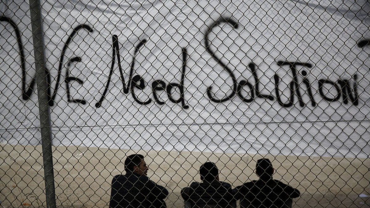 Immigranter sittandes under en banner utanför den tidigare olympiska stadion i södra Aten i december 2015. 