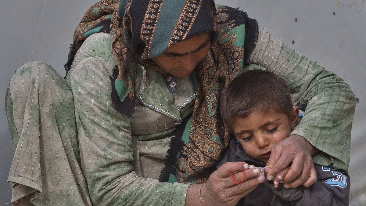En man från Kobane som filar naglarna på ett barn på ett flyktingläger. 

