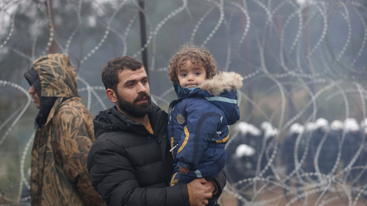 En pappa och hans barn vid taggtrådsstängslet som skiljer Belarus från EU-landet Polen. De senaste åren har Polen sett en ökning av migranter vid gränsen. Bild tagen i november 2021.