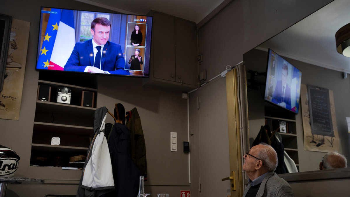 En man sitter på en krog i Marseille och följer den direktsända intervjun med president Macron.