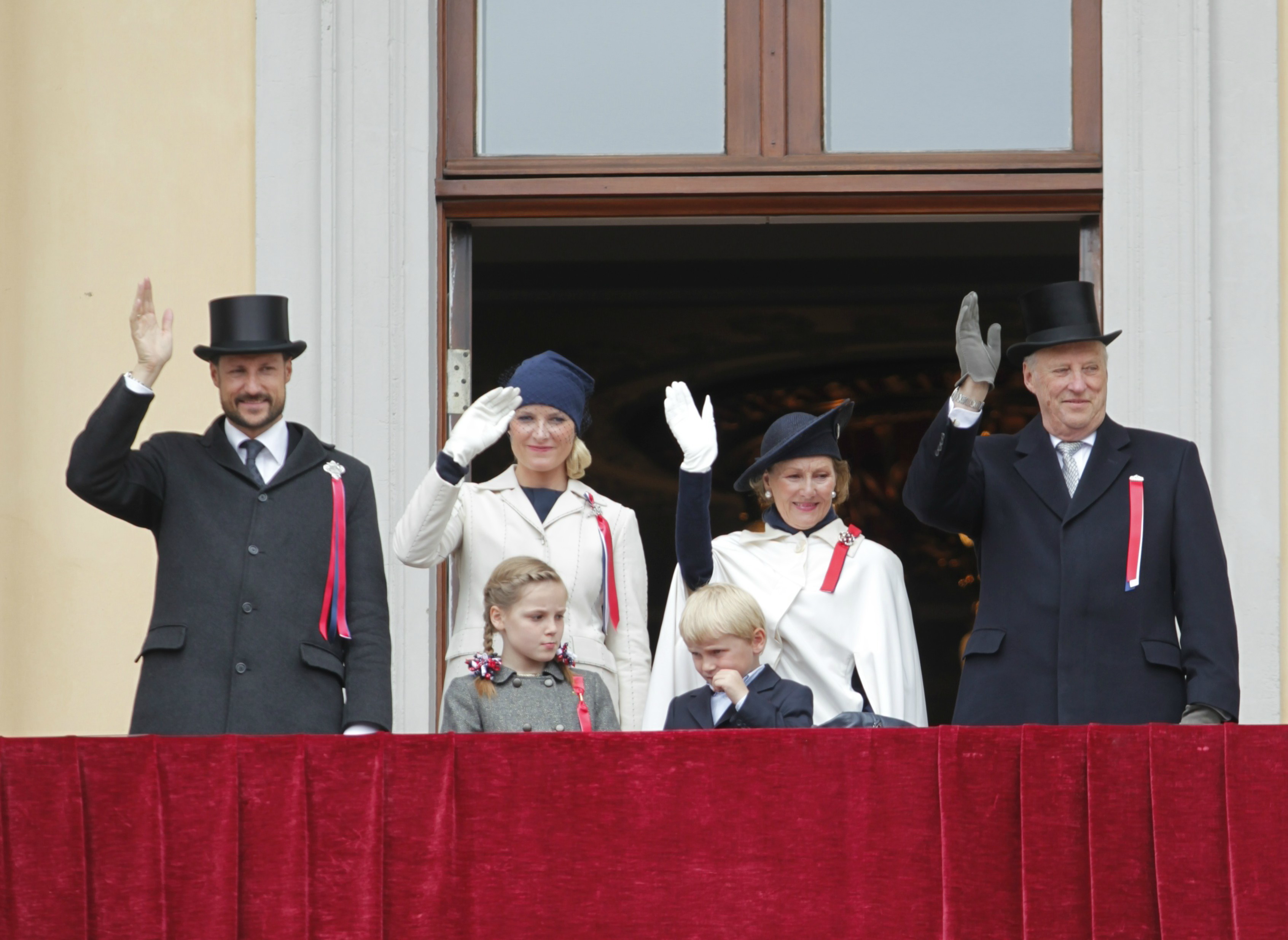 Kronprins Haakon, kronprinsessan Mette Marit, prins Sverre Magnus, drottning Sonja och Kung Harald hälsar på allmänheten utanför slottet.