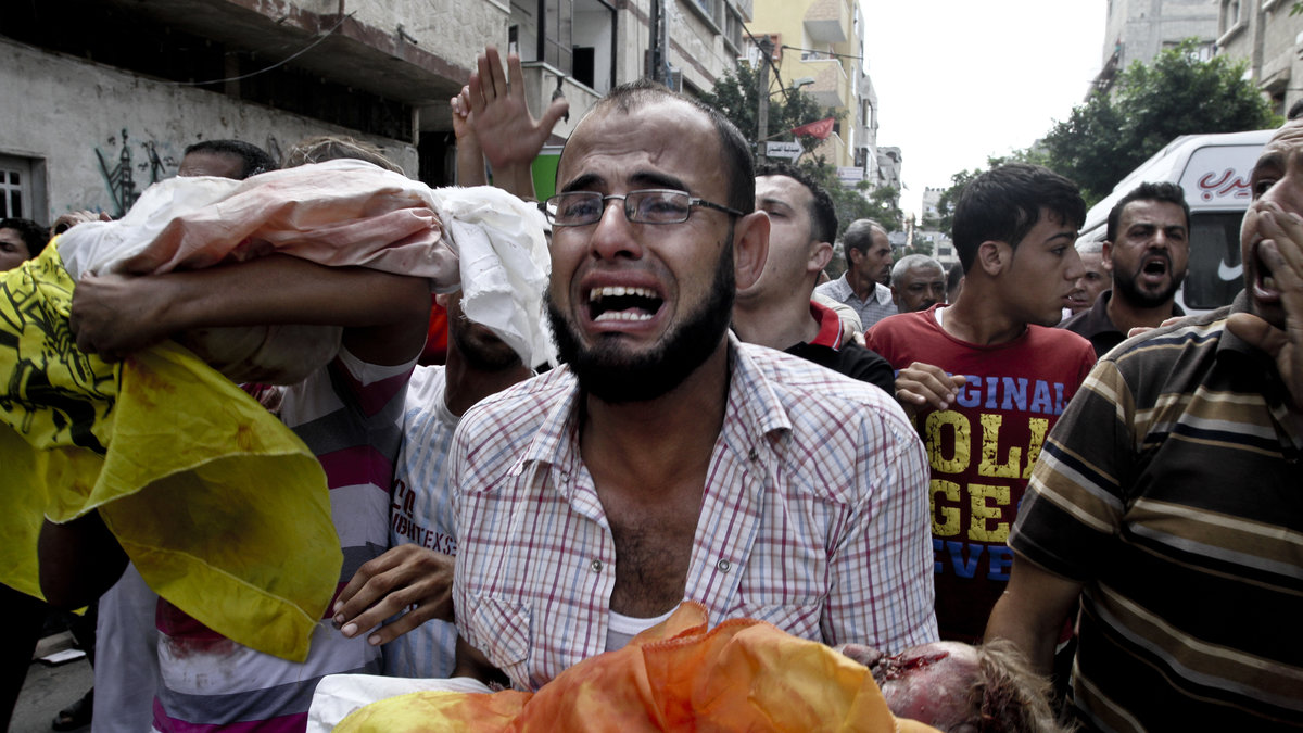 En gråtande far bär sitt barn som avlidit efter bombningar. 
