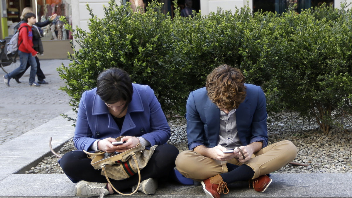 Två unga personer som stirrar ner i sina smartphones.