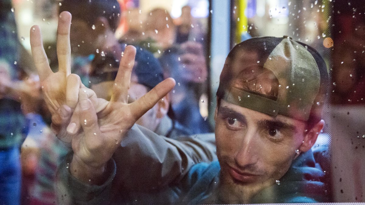 En man på flykt gör segertecken bakom ett bussfönster när bussen lämnar tågstationen i Saalfeld, Tyskland. 