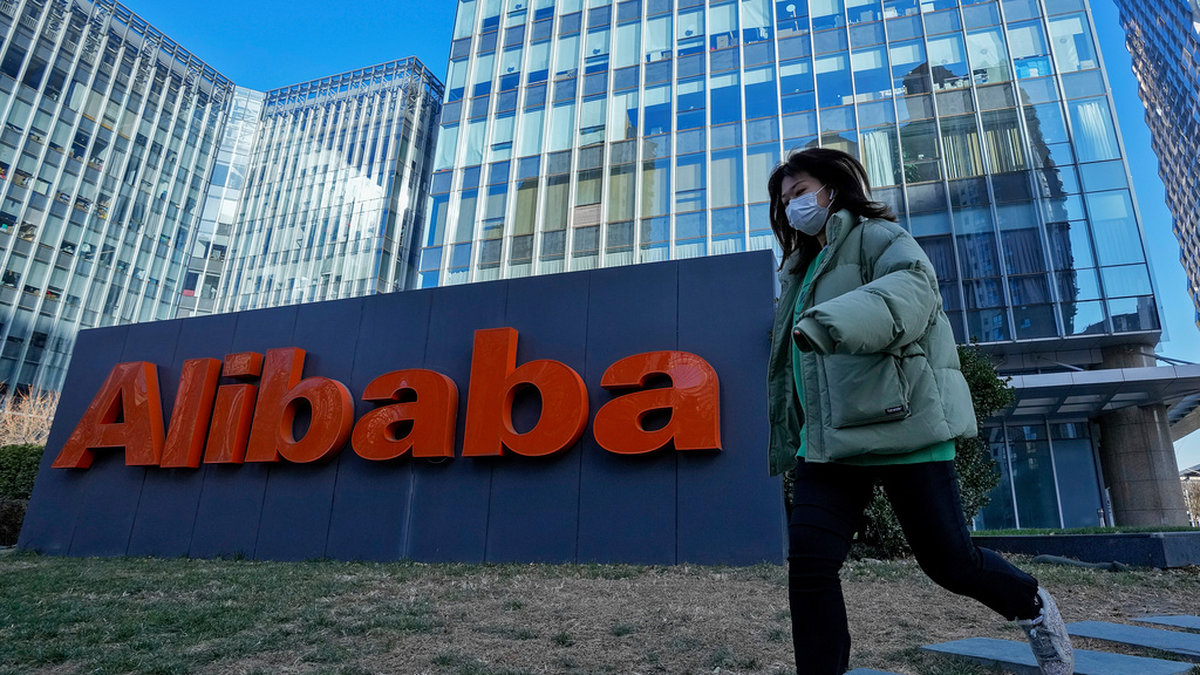 En kvinna i munskydd framför Alibabas lokaler i Peking. Arkivbild.