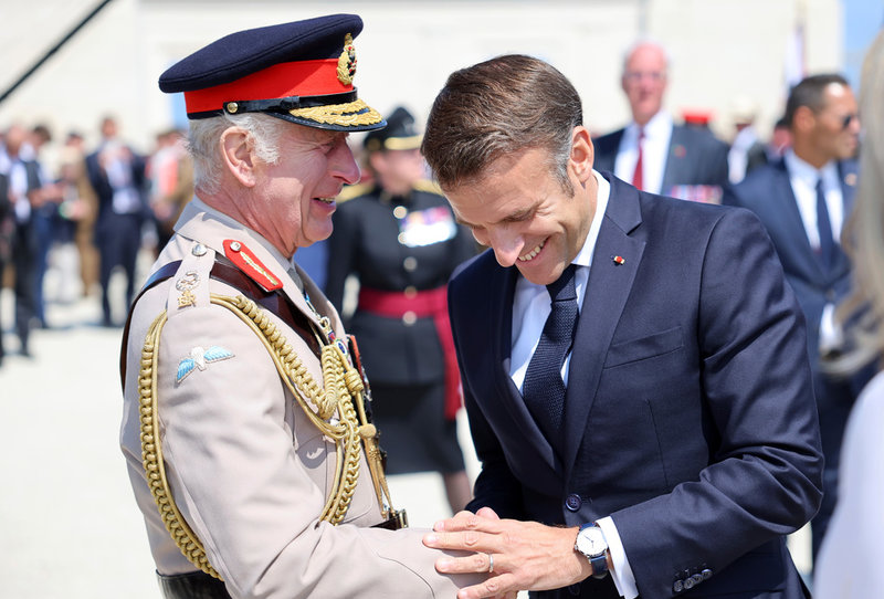 Storbritanniens kung Charles III och Frankrikes president Emmanuel Macron hälsar på varandra i Ver-Sur-Mer.