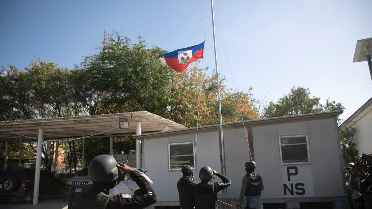Poliser gör honnör vid Haitis flagga som halats på halv stång i Port-au-Prince.