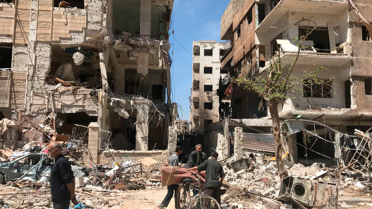 Människor står vid raserade byggnader i Douma den 16 april 2018, en dryg vecka efter klorgasattacken som dödade tiotals människor där. Arkivbild.