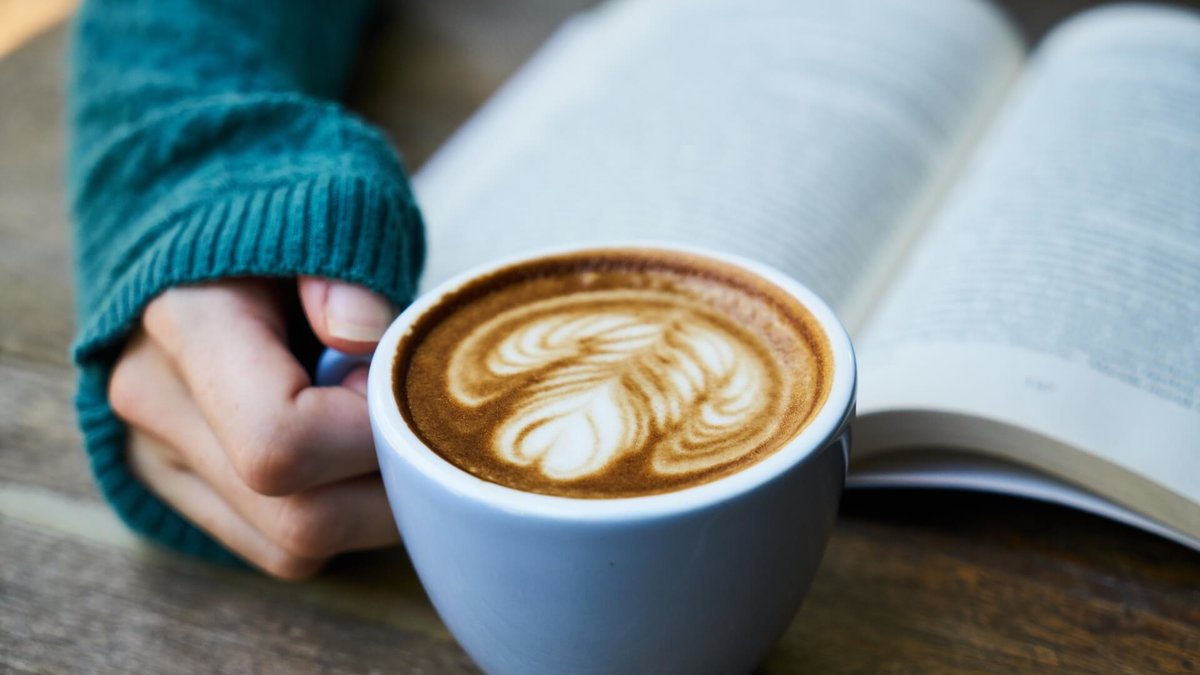 Kaffe latte står någon som läser en bok.