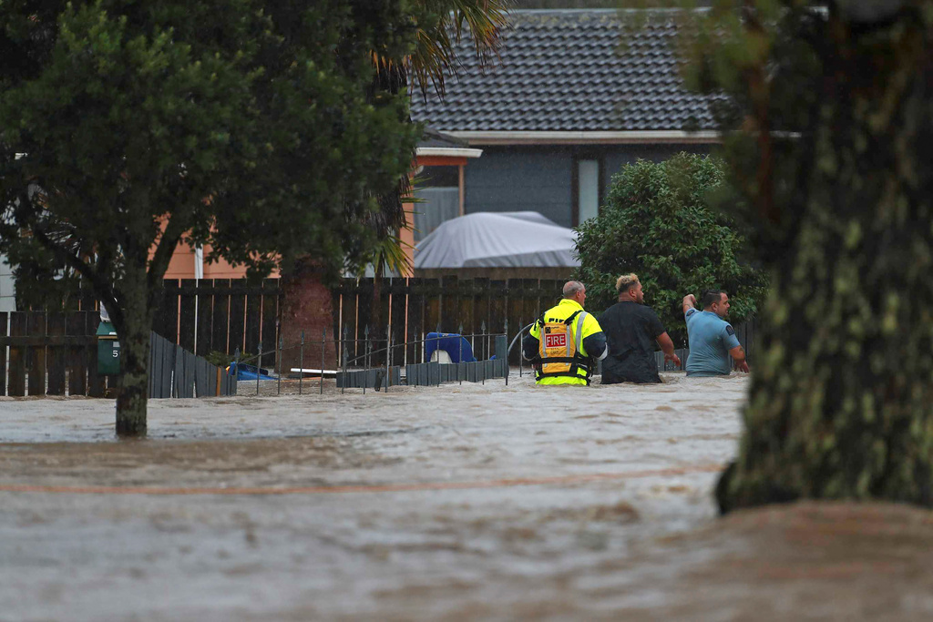 Personal från räddningstjänsten och en civilperson vadar genom vattenmassorna i Auckland på fredagen.