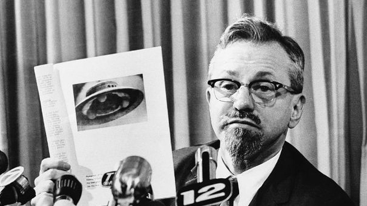 Astrofysikern J. Allen Hynek håller upp en bild på ett påstått UFO under en presskonferens i mars 1966 och blir tillfrågad av pressen vad han tror att bilden föreställer. J. Allen Hynek menade att det rörde sig om en bild på en hönsfoderautomat.