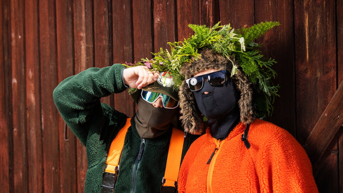 DJ Mårdhund (grön fleece, orangea hängslen) och Hooja (orange fleece) i duon Hooja lovar att vara ovanligt personliga när de debuterar som sommarpratare. Pressbild.