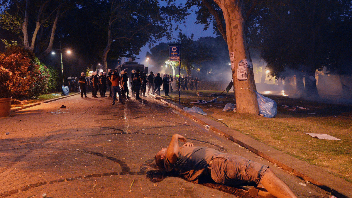En man vrider sig i plågor på marken. I bakgrunden skymtar kravallpolisen.