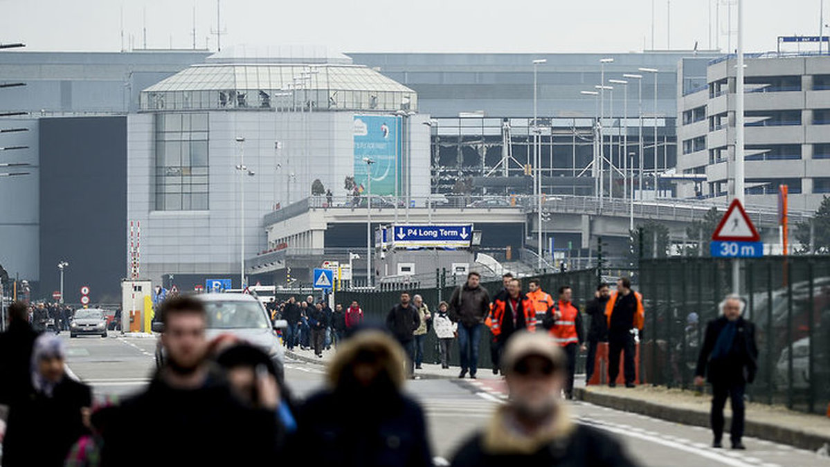 Människor evakueras från Zaventem.  I bakgrunden syns explosionens förödelse. 
