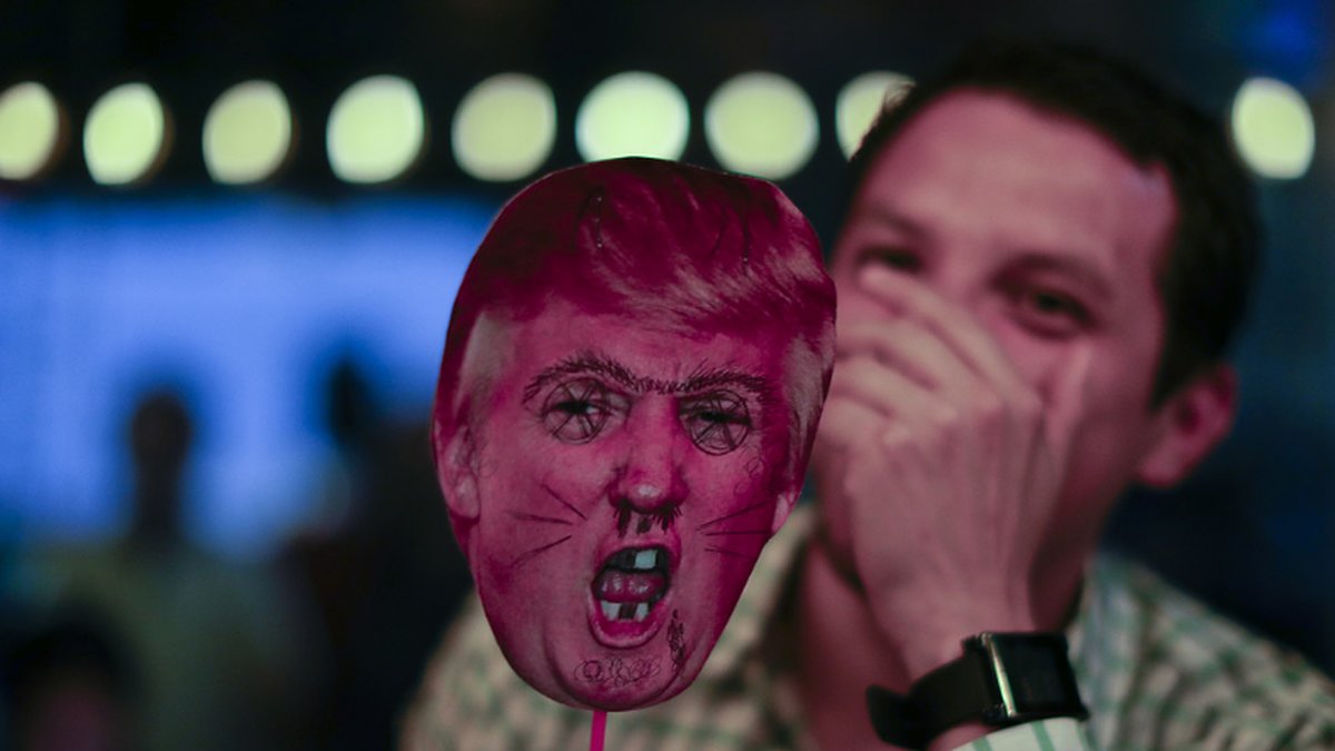 En man skrattar medan han håller upp en saboterad mask föreställande Donald Trump, i en bar i Buenos Aires, Argentina.